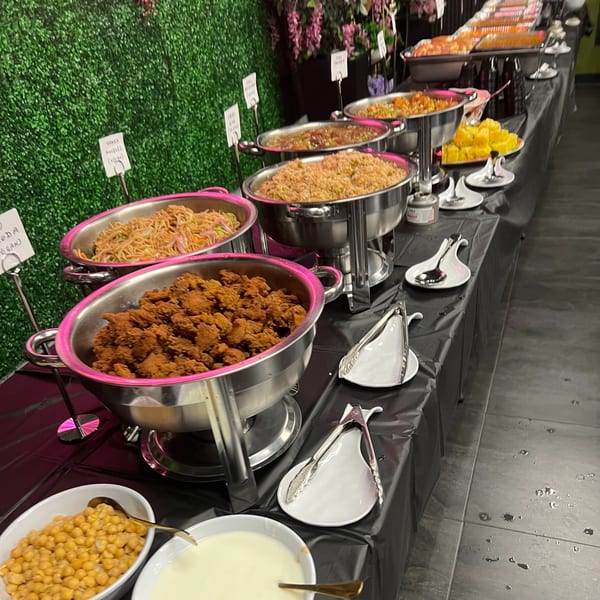 A Chaska Indian buffet table with chafing dishes of noodles, fried chicken, rice, and other dishes.
