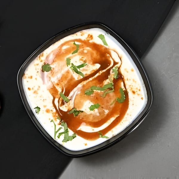 Overhead view of a square bowl of Chaska Dahi Bhalla, garnished with tamarind chutney and cilantro.
