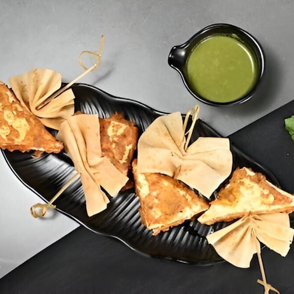 Chaska's Indian paneer pakora, triangular fried cheese fritters, served with green chutney on a black plate.
