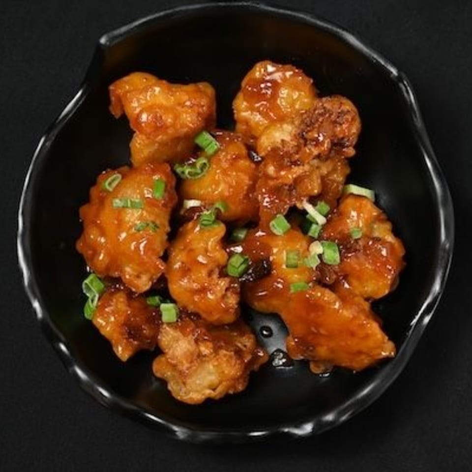 Chaska's Indian-style sweet and spicy cauliflower florets, garnished with green onions, in a black bowl.